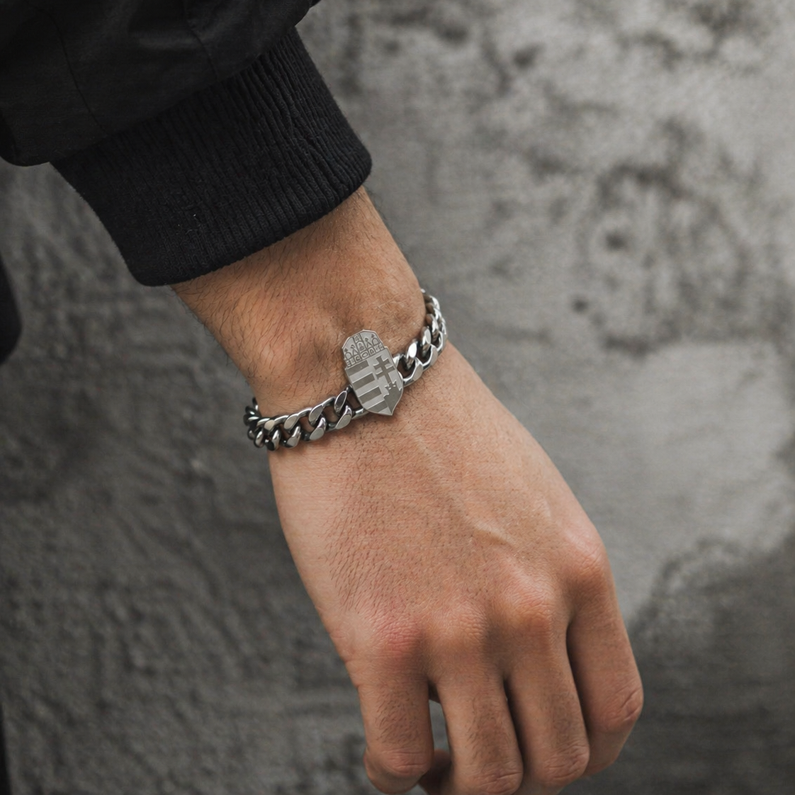 Silbernes Panzerarmband mit ungarischem Wappen-Element, getragen an einem männlichen Handgelenk vor grauer Betonwand
