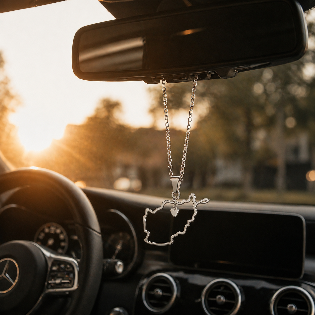 Silberner Auto-Rückspiegel-Anhänger mit Afghanistan-Karten-Kontur und kleinem Herz-Detail – hängend im Mercedes-Innenraum bei Sonnenuntergang