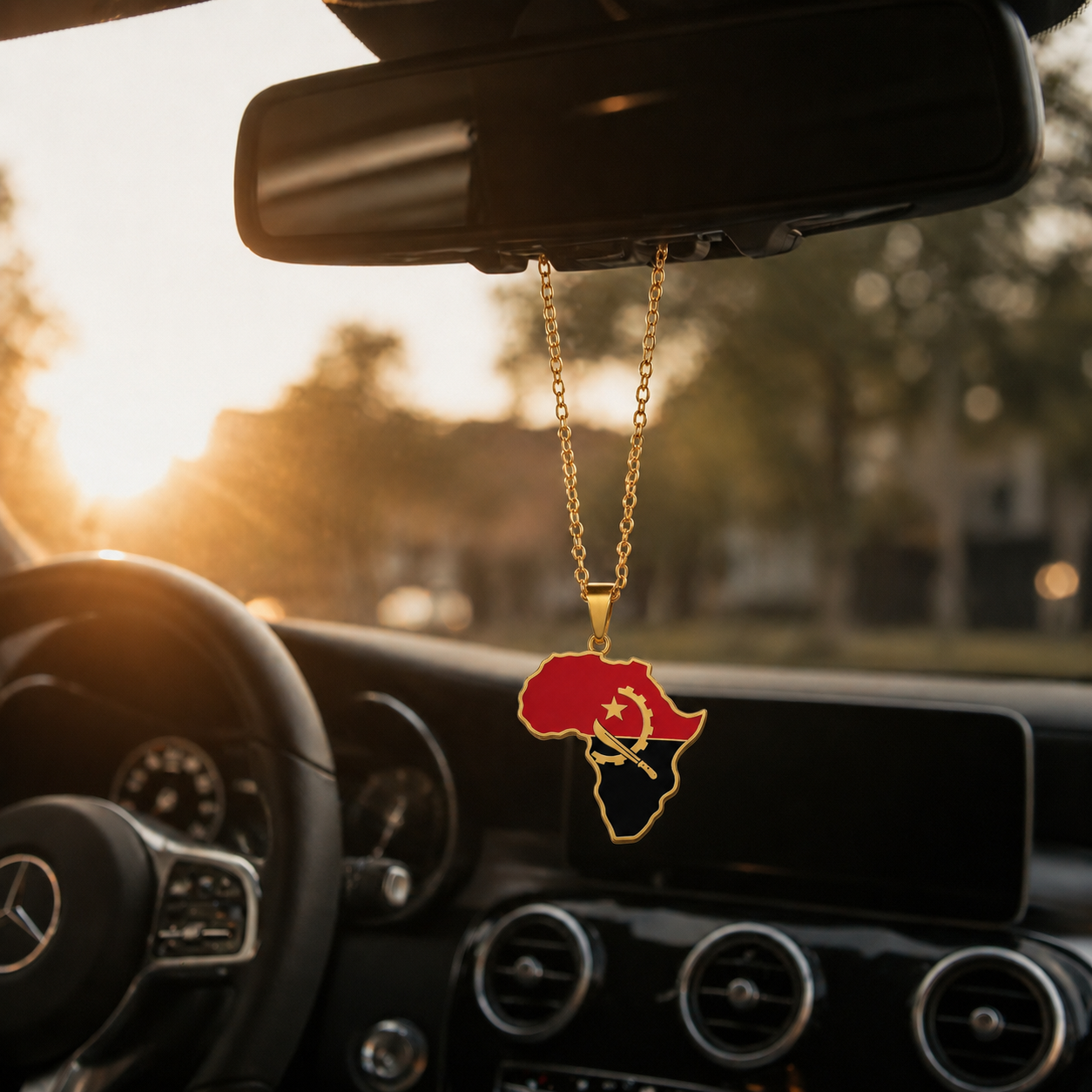 Goldener Afrika-Kontinent-Anhänger mit Angola-Flaggenfarben Rot, Schwarz und goldenem Emblem – hängend am Rückspiegel eines Mercedes bei warmem Sonnenuntergangslicht