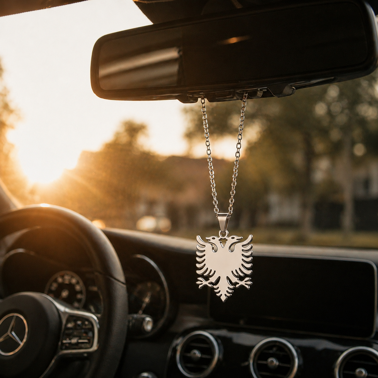 Silberner Auto-Rückspiegel-Anhänger mit mattiertem albanischem Doppeladler-Motiv ohne Steinbesatz – hängend im Mercedes-Innenraum bei Sonnenuntergang