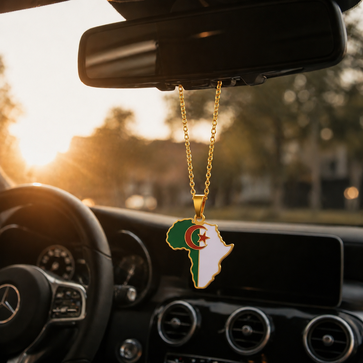 Goldener Auto-Rückspiegel-Anhänger mit Afrika-Karten-Motiv in den algerischen Landesfarben Grün und Weiß mit rotem Halbmond und Stern – hängend im Mercedes-Innenraum bei Sonnenuntergang