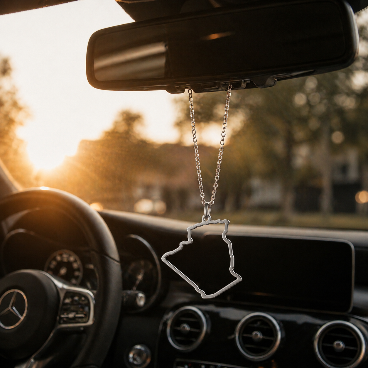Silberner Auto-Rückspiegel-Anhänger mit Algerien-Karten-Kontur ohne Farbfüllung – hängend im Mercedes-Innenraum bei Sonnenuntergang