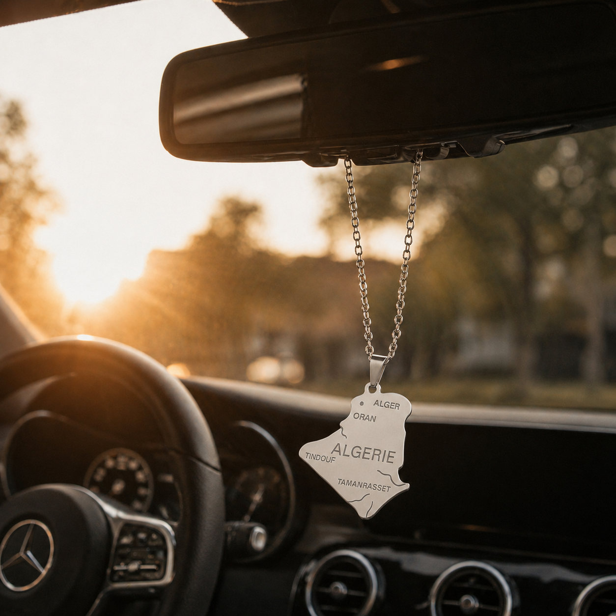 Silberner Auto-Rückspiegel-Anhänger mit Algerien-Karten-Motiv und gravierten Städtenamen wie Alger, Oran und Tamanrasset – hängend im Mercedes-Innenraum bei Sonnenuntergang