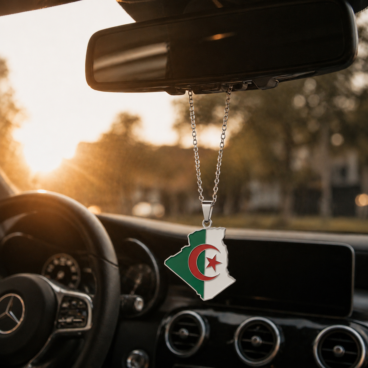 Silberner Auto-Rückspiegel-Anhänger mit Algerien-Karten-Motiv in den Landesfarben Grün und Weiß mit rotem Halbmond und Stern – hängend im Mercedes-Innenraum bei Sonnenuntergang