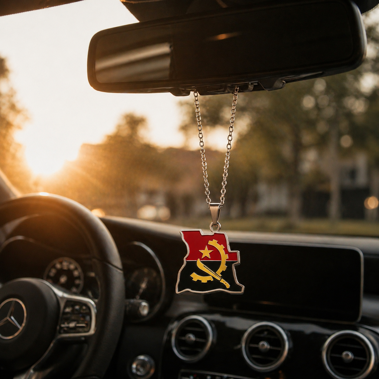 Angola-Karten-Anhänger mit Flaggenfarben Rot, Schwarz und goldenem Emblem – hängend am Rückspiegel eines Mercedes bei warmem Sonnenuntergangslicht