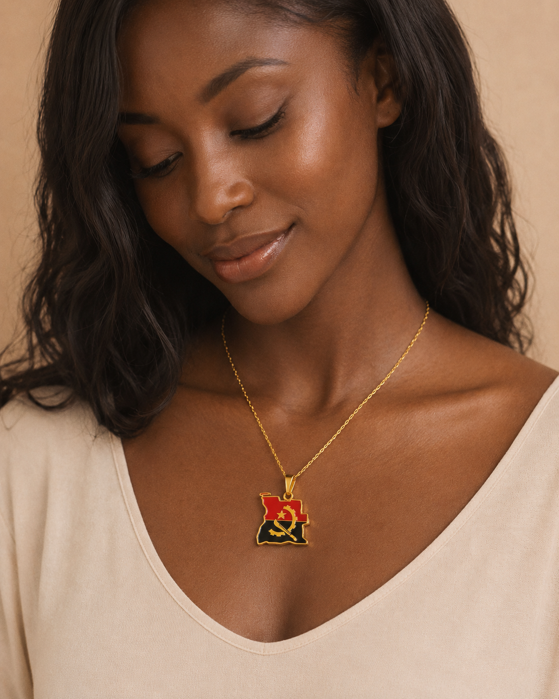 Goldene Angola-Karten-Halskette mit Flaggenfarben Rot, Schwarz und goldenem Emblem – getragen von einer jungen Frau im beigen Top, Studio-Porträt vor warmem Hintergrund