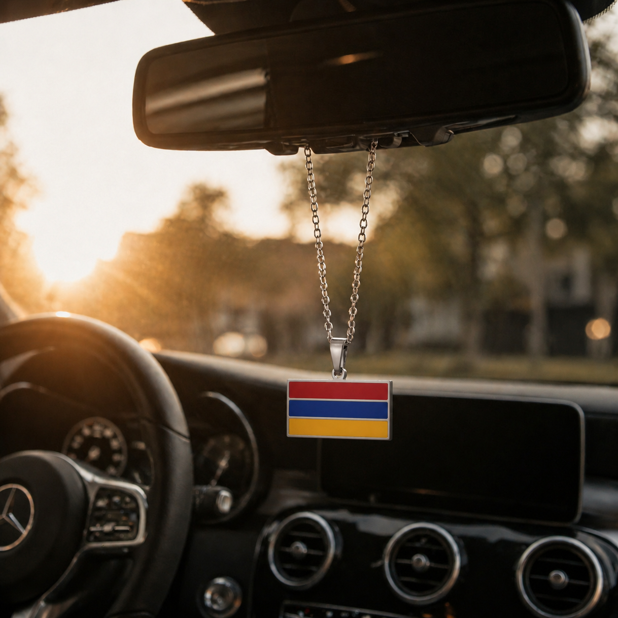 Silberner armenischer Flaggen-Anhänger in den Landesfarben Rot, Blau und Gelb, hängend am Rückspiegel eines Mercedes im warmen Sonnenuntergangslicht