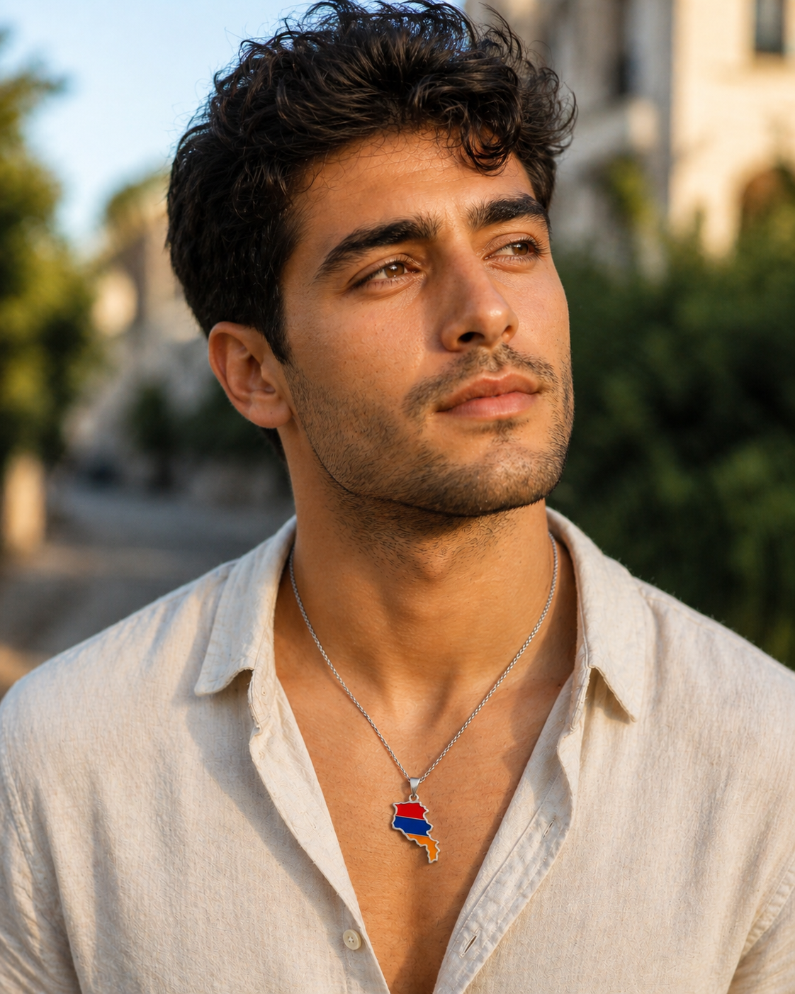 Silberne Halskette mit Armenien-Karten-Anhänger in den Landesfarben Rot, Blau und Orange, getragen von einem Mann im cremefarbenen Leinenhemd, Outdoor-Porträt im warmen Sonnenlicht