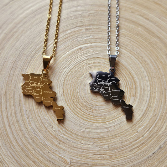 Zwei Halsketten mit Armenien-Karten-Anhänger mit gravierten Provinznamen in Gold und Silber, nebeneinander auf einer Holzscheibe liegend