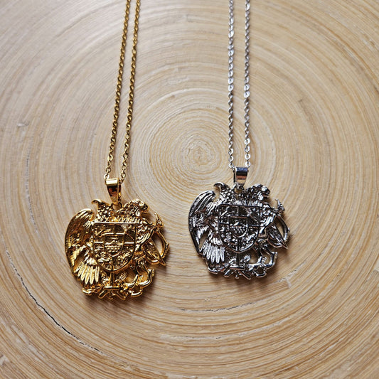 Zwei Halsketten mit armenischem Wappen-Anhänger mit Adler und Schild in Gold und Silber, nebeneinander auf einer Holzscheibe liegend