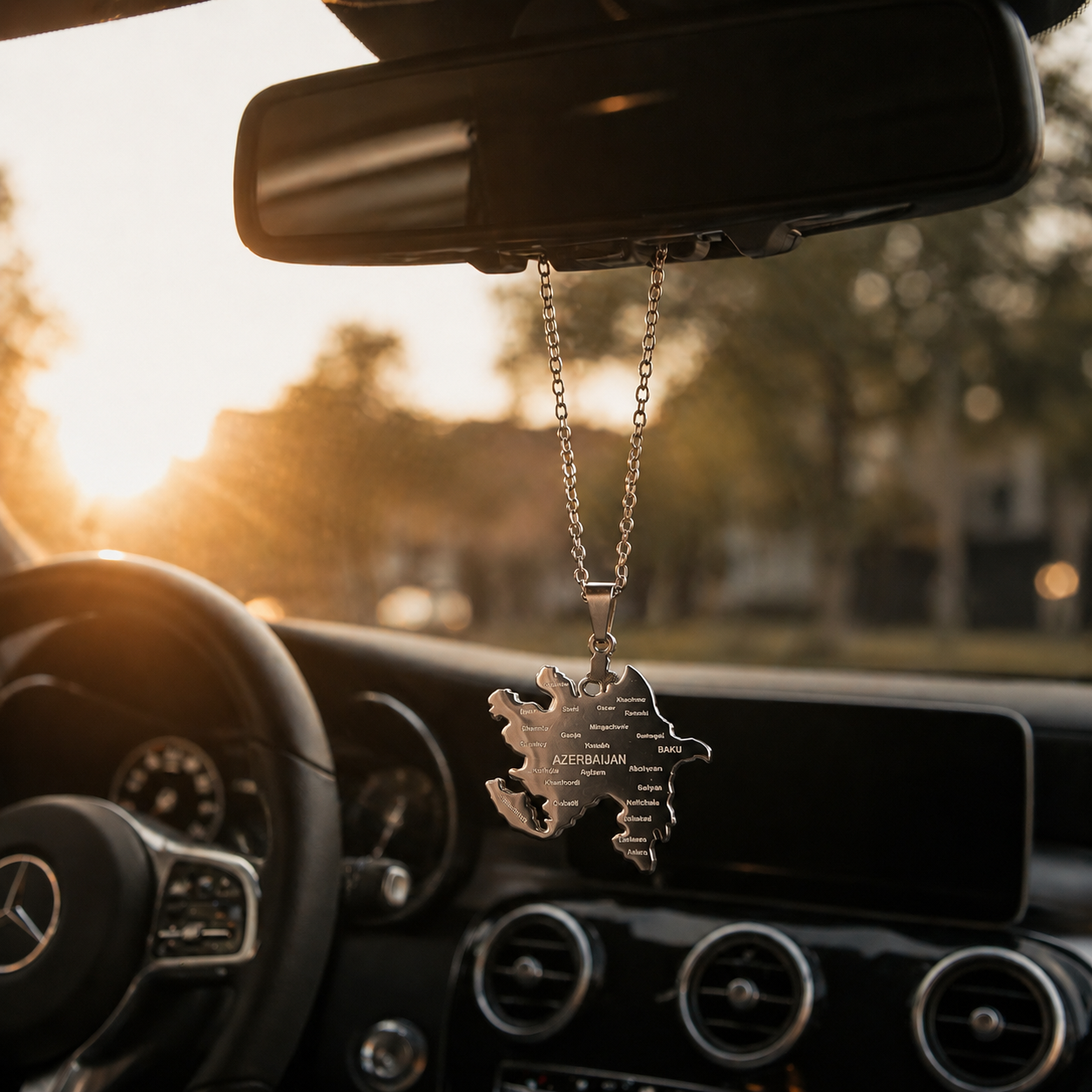 Silberner Auto-Rückspiegel-Anhänger mit Aserbaidschan-Karten-Motiv und gravierten Städtenamen wie Baku und Ganja – hängend im Mercedes-Innenraum bei Sonnenuntergang