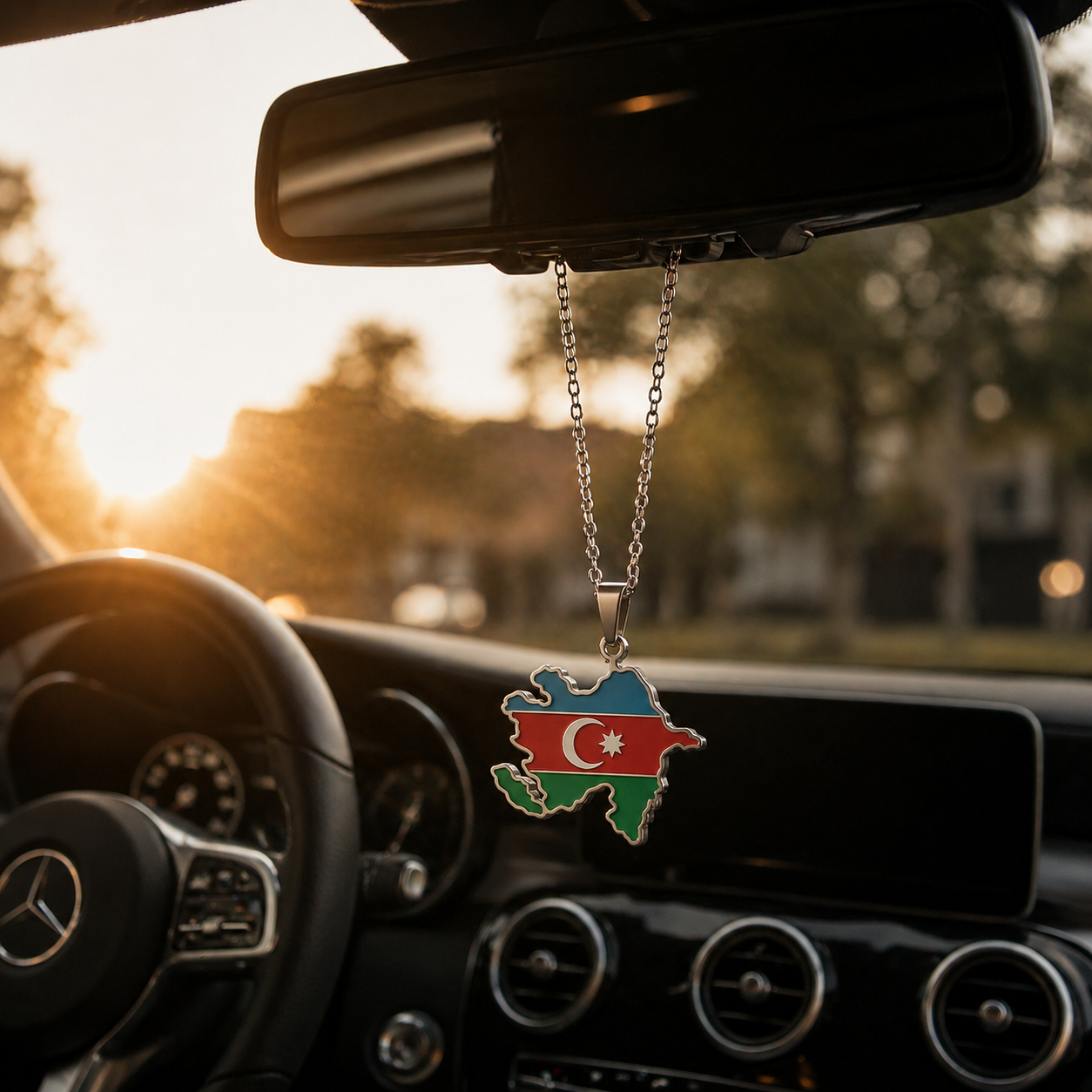 Silberner Auto-Rückspiegel-Anhänger mit Aserbaidschan-Karten-Motiv in den Landesfarben Blau, Rot und Grün mit Halbmond und Stern – hängend im Mercedes-Innenraum bei Sonnenuntergang