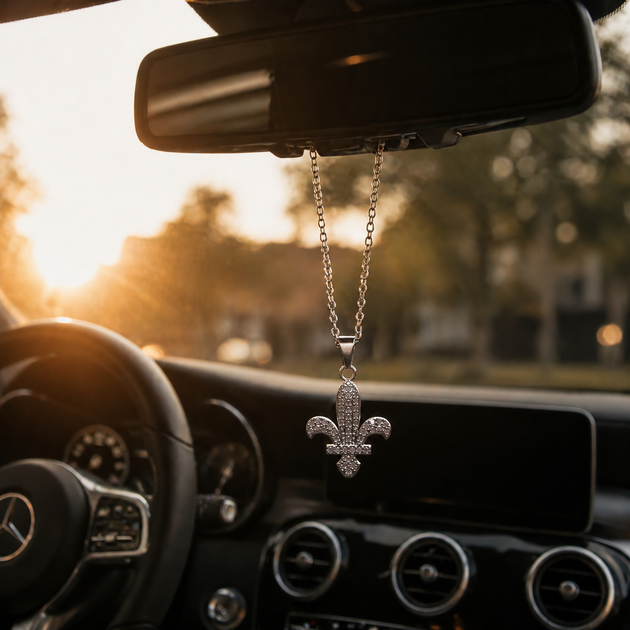 Silberner Auto-Rückspiegel-Anhänger mit Bosnischer-Lilien-Motiv und Zirkonia-Steinen besetzt – hängend im Mercedes-Innenraum bei Sonnenuntergang