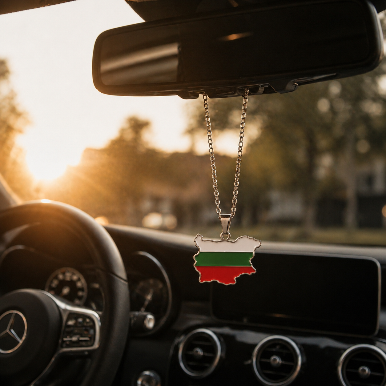 Silberner Auto-Rückspiegel-Anhänger mit Bulgarien-Karten-Motiv in den Landesfarben Weiß, Grün und Rot – hängend im Mercedes-Innenraum bei Sonnenuntergang