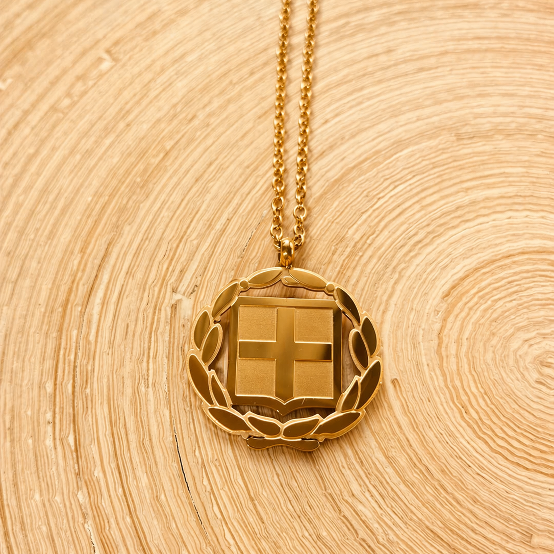 Griechischer Wappen Anhänger in Gold – Nahaufnahme mit Kreuz und Lorbeerkranz auf Holzuntergrund