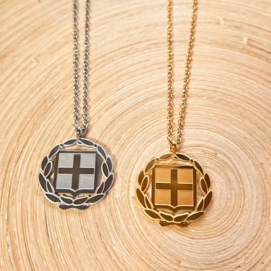 Griechische Wappen Halskette in Silber und Gold – beide Varianten mit Kreuz und Lorbeerkranz auf Holzuntergrund im Vergleich