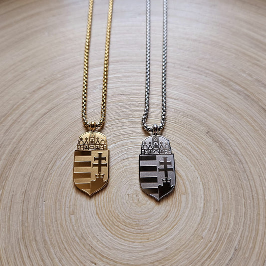 Zwei Halsketten mit ungarischem Wappen-Anhänger in Gold und Silber, nebeneinander auf einer Holzscheibe liegend
