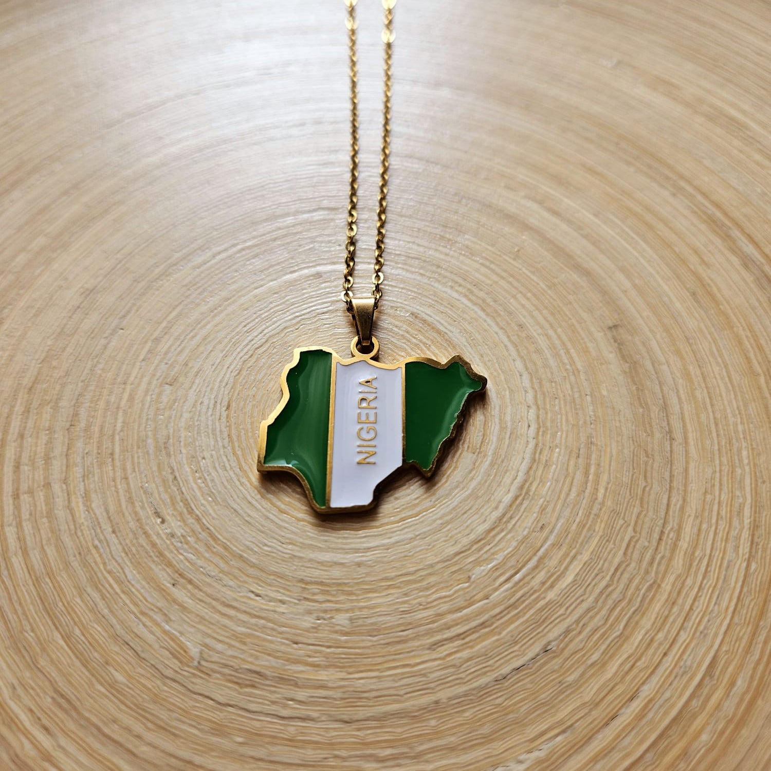 Nigeria Karte Flagge Anhänger in Gold – Nahaufnahme mit NIGERIA Schriftzug und grün-weißer Flagge auf Holzuntergrund