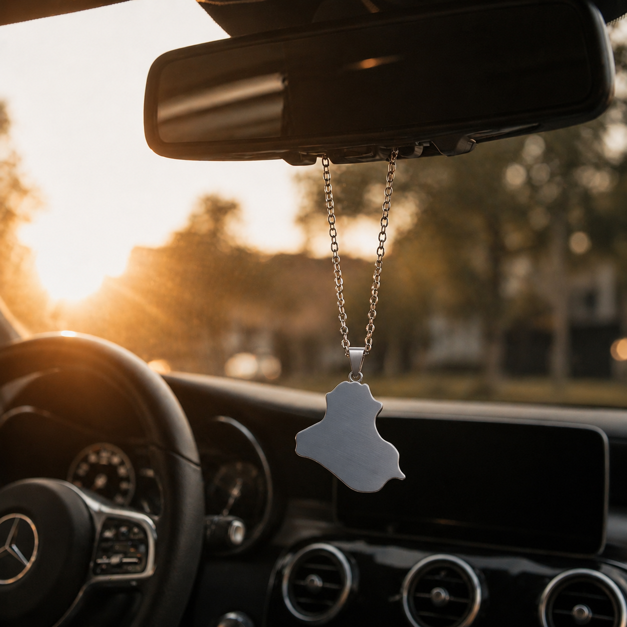 Silberner Auto-Rückspiegel-Anhänger mit mattiertem Irak-Karten-Motiv ohne Farbfüllung – hängend im Mercedes-Innenraum bei Sonnenuntergang