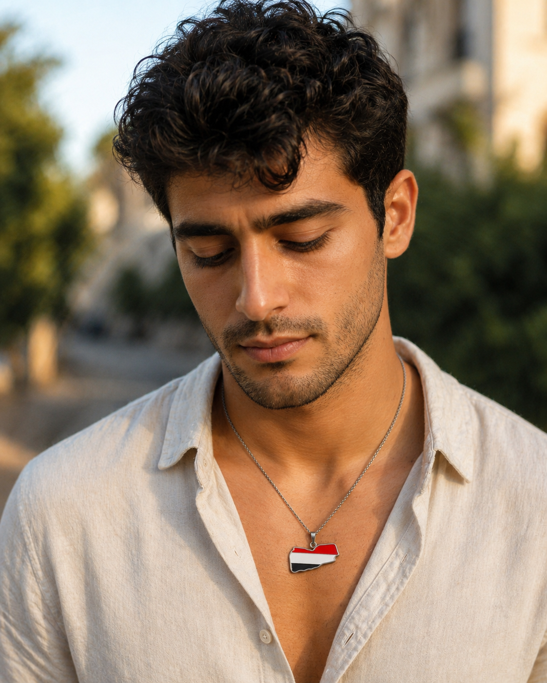 Silberne Jemen-Karten-Halskette mit Flaggenfarben Rot, Weiß und Schwarz – getragen von einem jungen Mann im weißen Leinenhemd, Outdoor-Porträt bei Sonnenuntergang