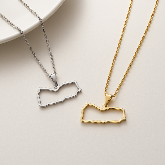 Zwei filigrane Jemen-Karten-Halsketten als offene Kontur aus Edelstahl – eine in Silber und eine in Gold – nebeneinander auf hellem Hintergrund