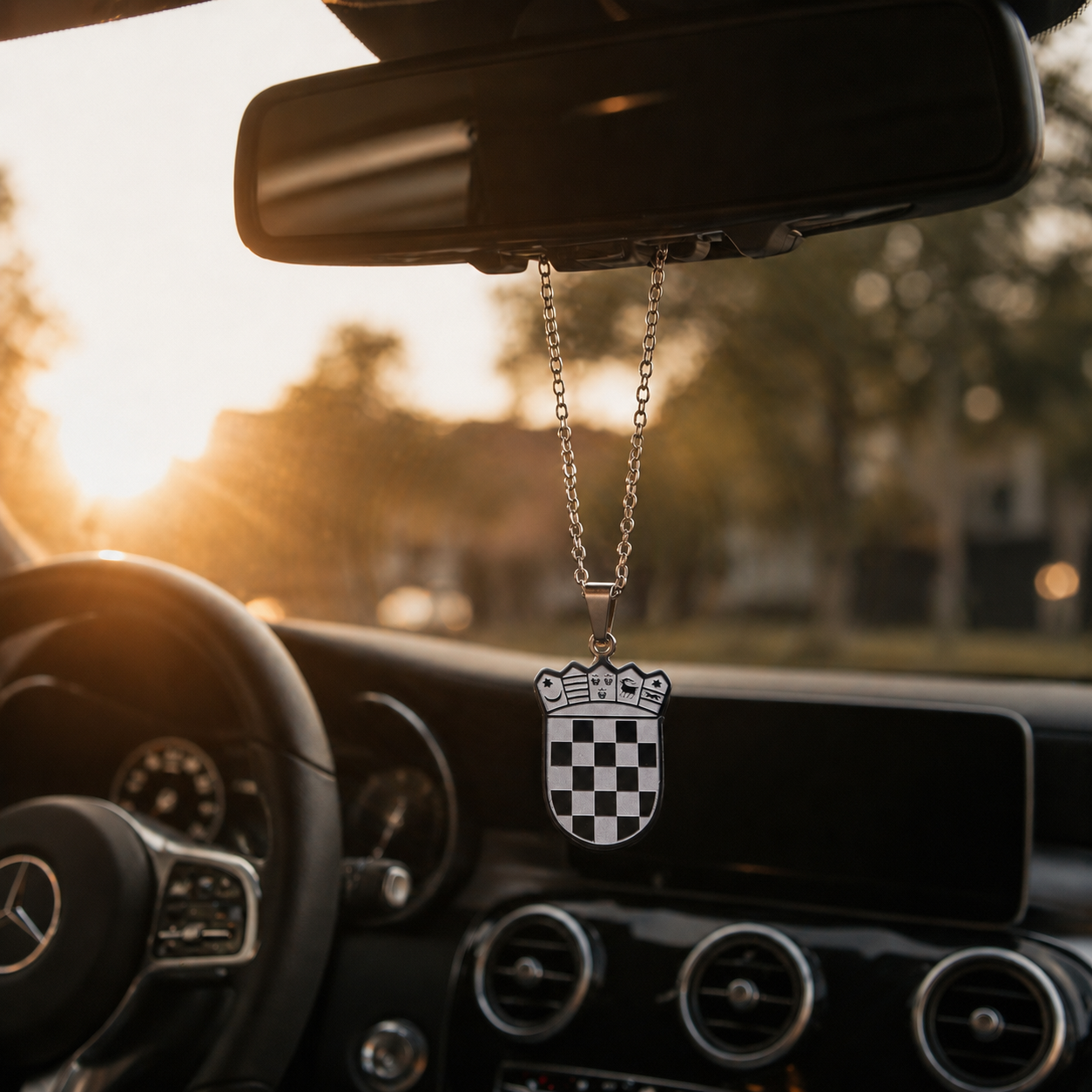 Silberner kroatischer Wappen-Anhänger mit Schachbrettmuster und Krone, hängend am Rückspiegel eines Mercedes im warmen Sonnenuntergangslicht