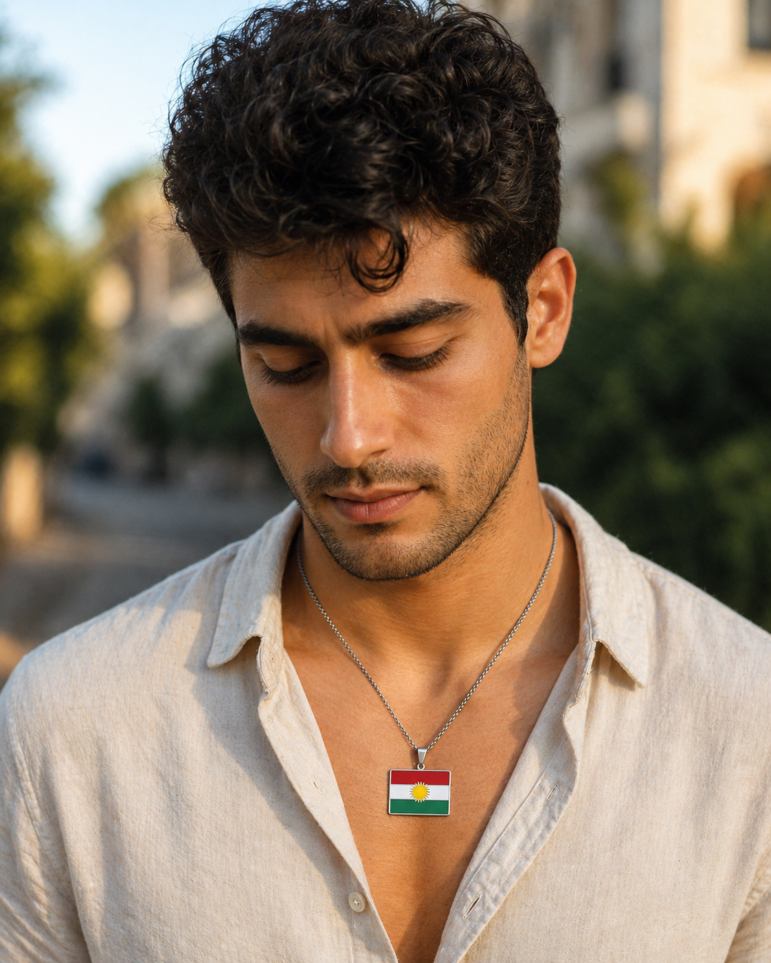 Kurdistan-Flaggenanhänger aus Edelstahl in Silber, rechteckig – getragen von einem jungen Mann im beigen Leinenhemd, Outdoor-Porträt bei Sonnenuntergang