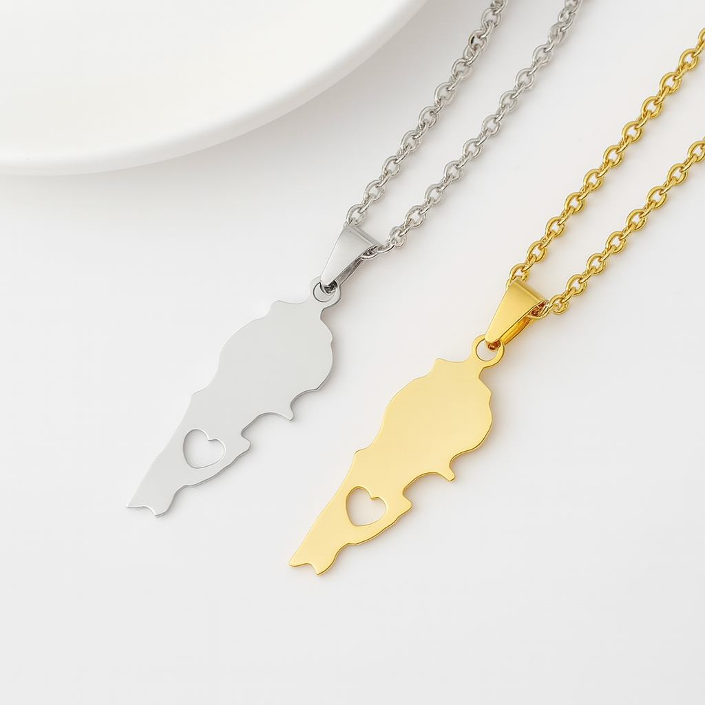 Zwei Halsketten mit Libanon-Karten-Anhänger mit ausgestanztem Herz in Gold und Silber, nebeneinander auf hellem Hintergrund liegend