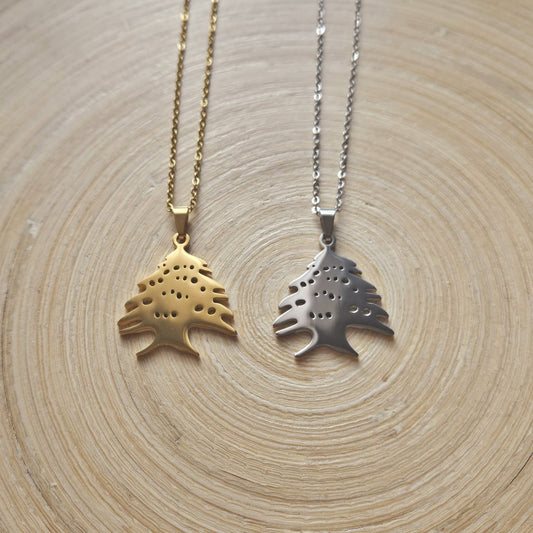 Zwei Halsketten mit libanesischer Zeder-Anhänger in Gold und Silber, nebeneinander auf einer Holzscheibe liegend