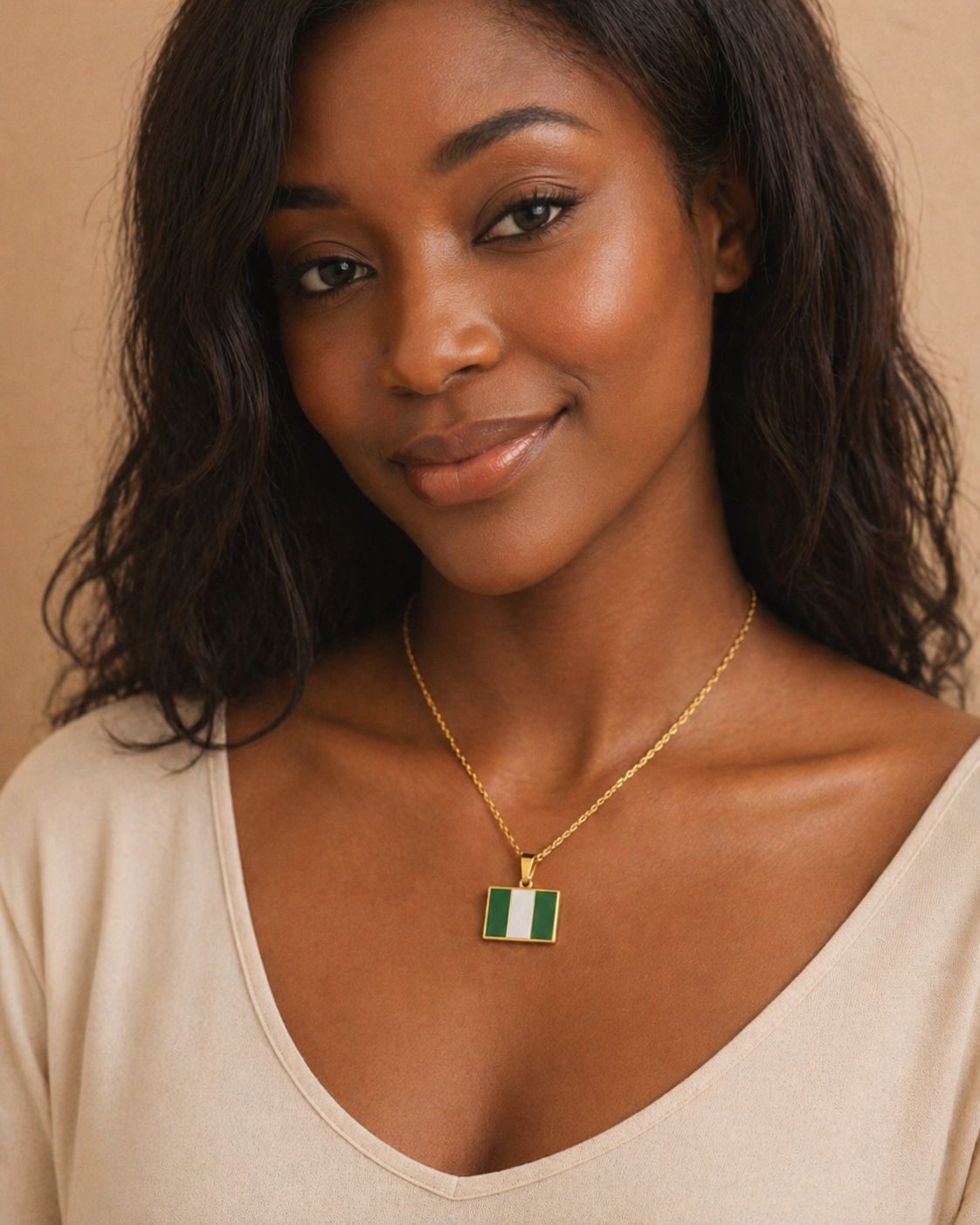 Goldene Halskette mit nigerianischer Flagge als Anhänger, getragen von einer lächelnden Frau im beigen Top, Studio-Porträt vor warmem Hintergrund