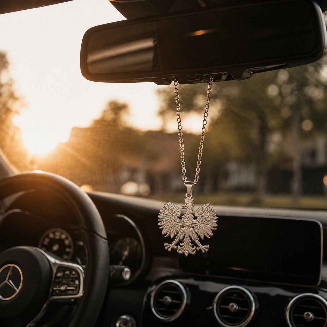 Silberne Polen Adler Halskette aus Edelstahl hängt als modernes Auto Accessoire am Rückspiegel eines Mercedes bei Sonnenuntergang.