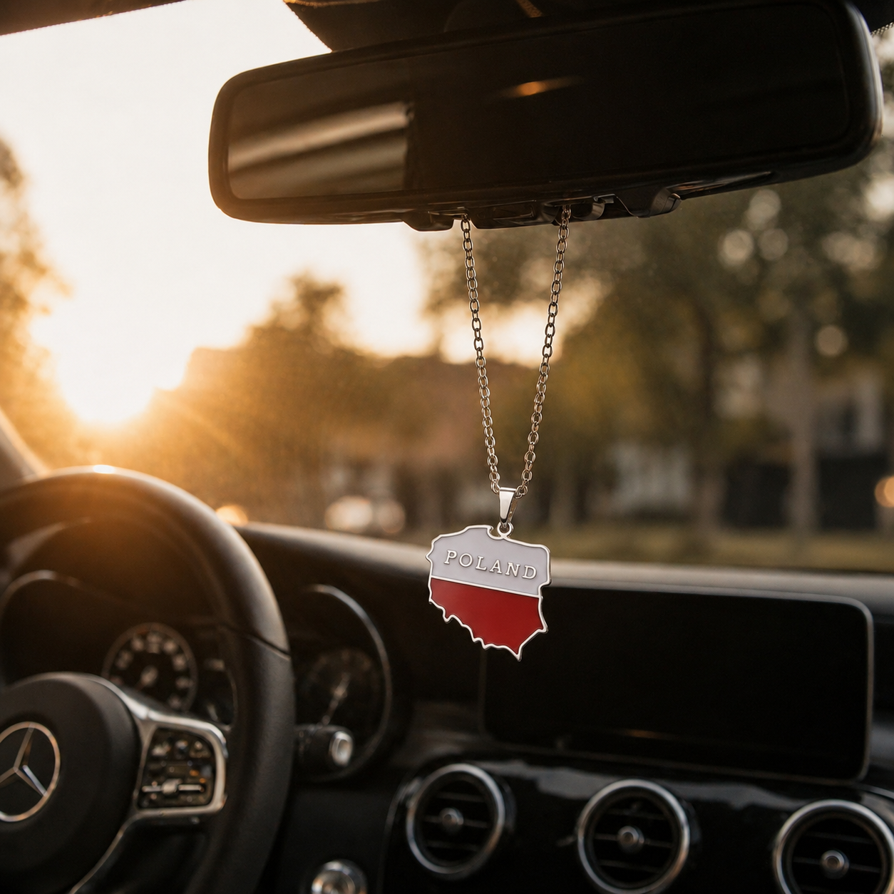 Polen-Karten-Anhänger in den Landesfarben Weiß und Rot mit Schriftzug "Poland" an silberner Kette, hängend am Rückspiegel eines Mercedes im warmen Sonnenuntergangslicht