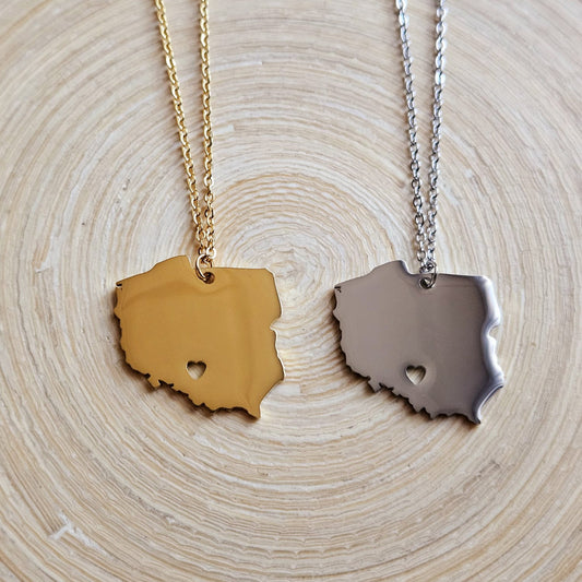 Zwei Halsketten mit massivem Polen-Karten-Anhänger mit ausgestanztem Herz – in Gold und Silber – nebeneinander auf einer Holzscheibe liegend