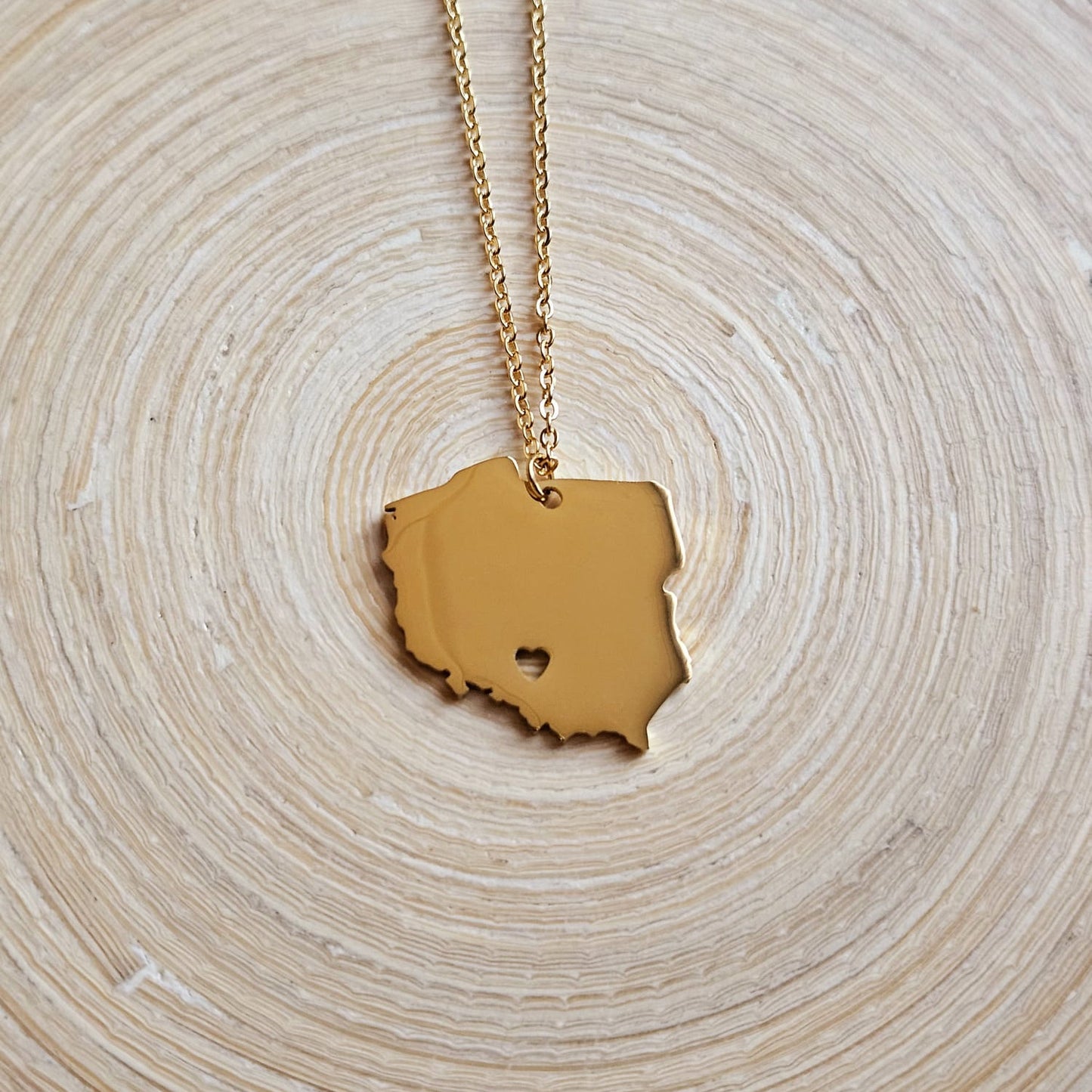 Goldene Halskette mit massivem Polen-Karten-Anhänger mit ausgestanztem Herz, auf einer Holzscheibe liegend
