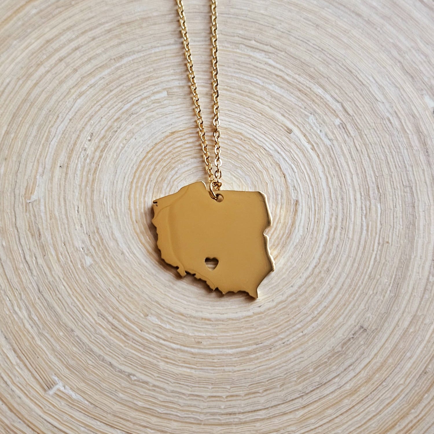 Goldene Halskette mit massivem Polen-Karten-Anhänger mit ausgestanztem Herz, auf einer Holzscheibe liegend