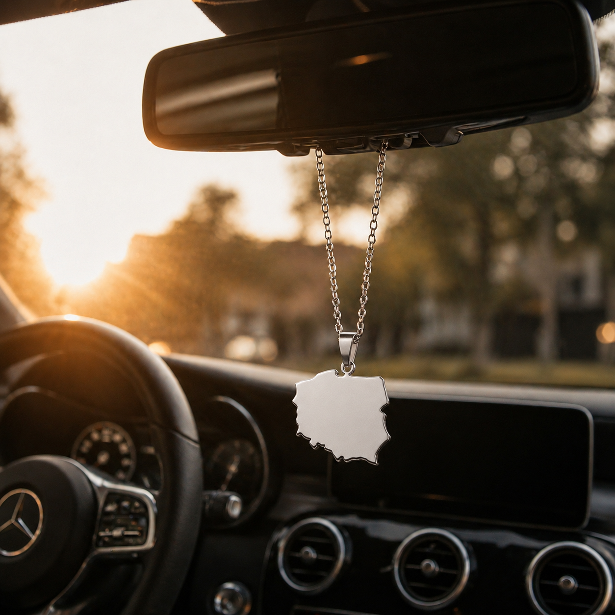 Silberne Polen Landkarten Halskette aus Edelstahl hängt als modernes Auto Accessoire am Rückspiegel eines Mercedes bei Sonnenuntergang.