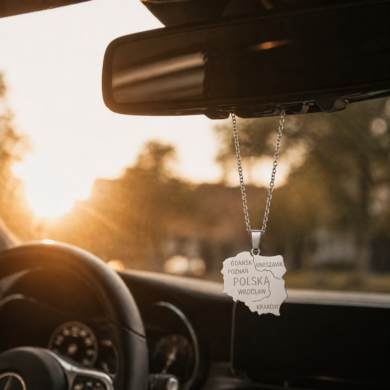 Silberne Polen Landkarten Halskette aus Edelstahl mit Städte Gravur hängt als stilvolles Auto Accessoire am Rückspiegel eines Mercedes bei Sonnenuntergang.