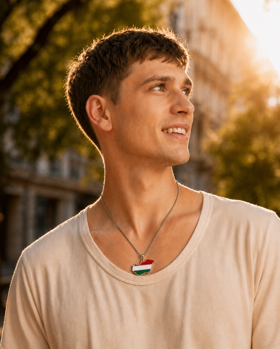 Silberne Halskette mit Ungarn-Karten-Anhänger in den Landesfarben Rot, Weiß und Grün, getragen von einem lächelnden Mann im beigen T-Shirt, Outdoor-Porträt im warmen Sonnenuntergangslicht